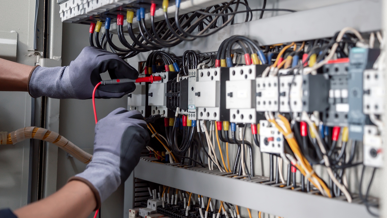 Electricians using a multimeter to measure the output of wires on a breaker box.