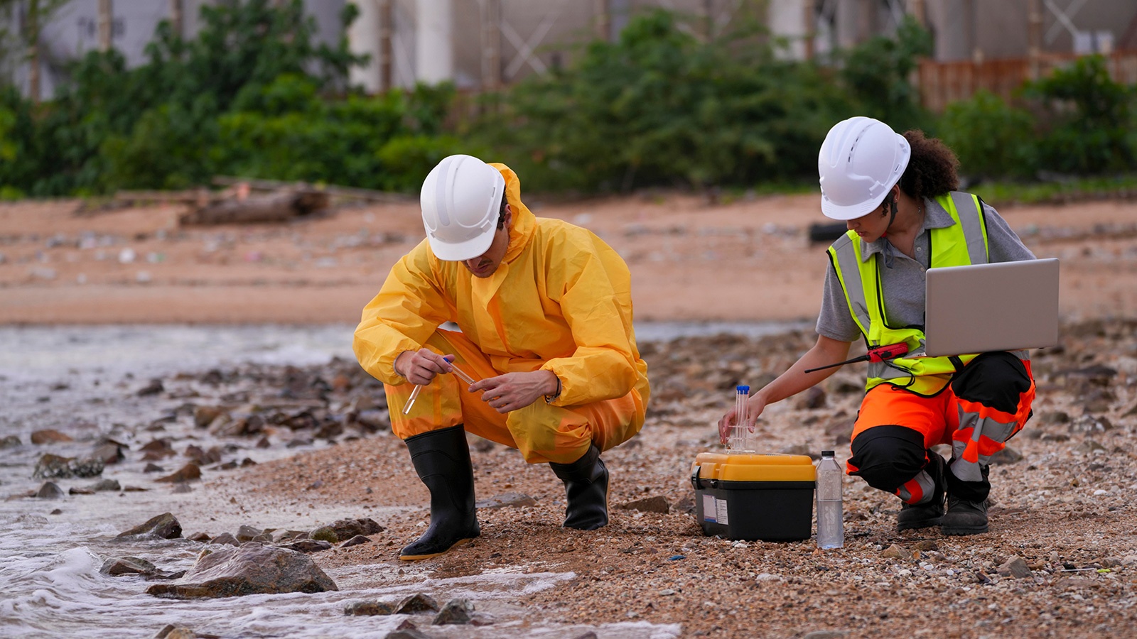 Two environmental scientists conduct coastal water sampling using test tubes and digital equipment