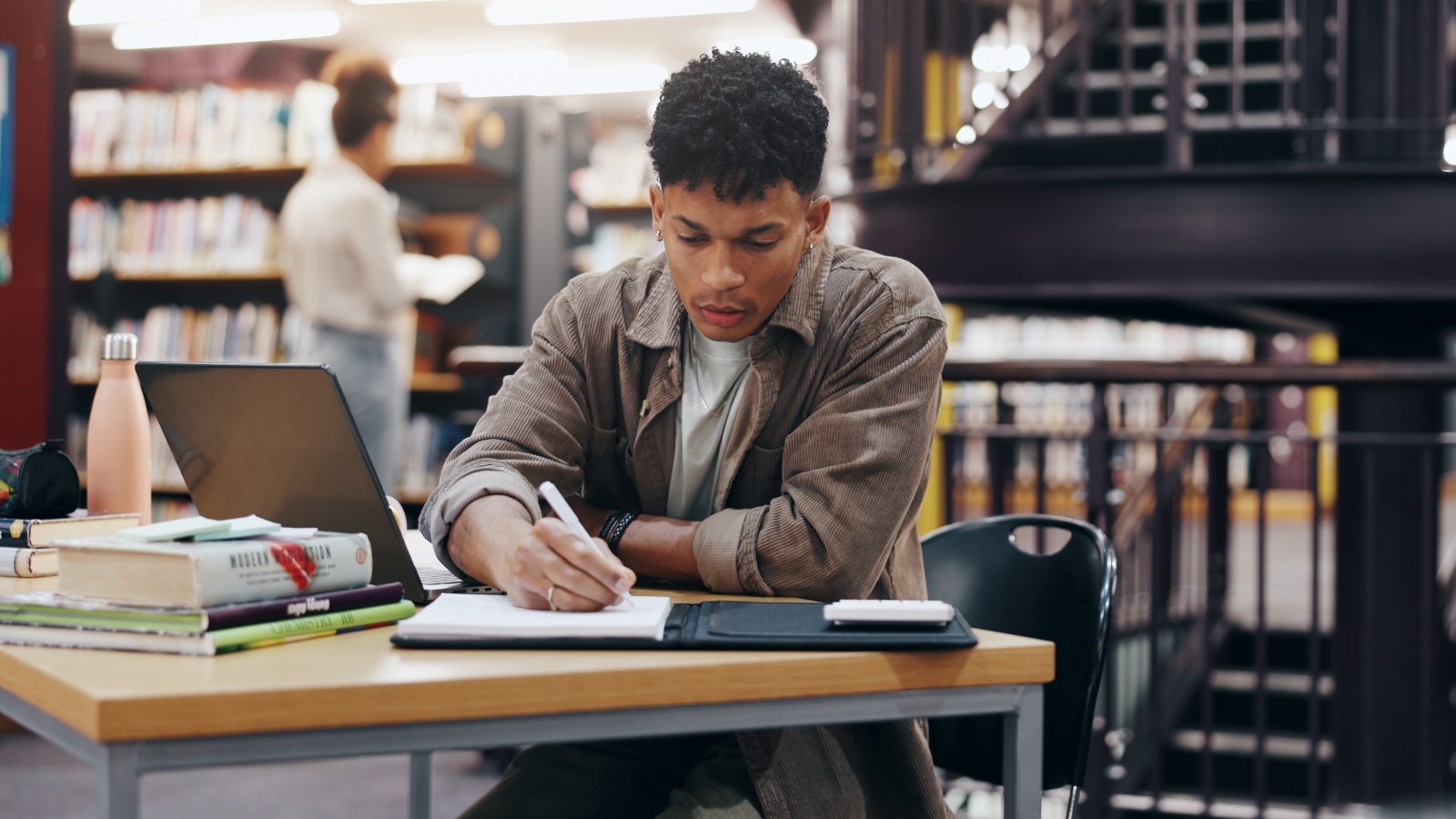 A student writes in their notepad while studying in the library.