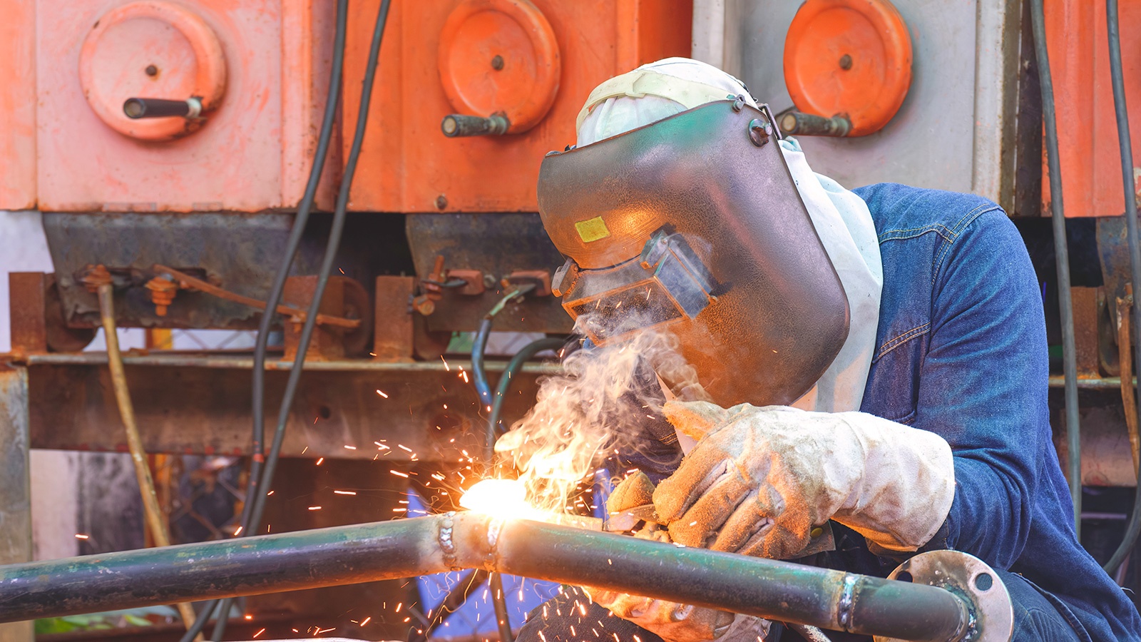 Welder with safety equipment is welding steel pipe at workshop