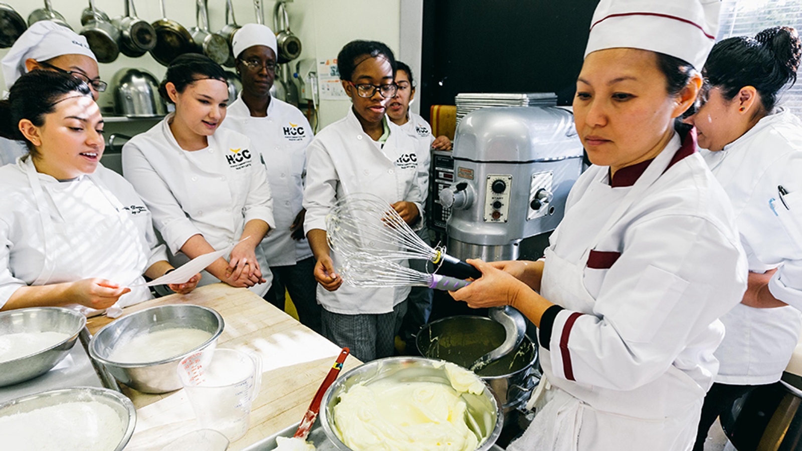 Pastry students observing as their instructor demonstrates a baking technique