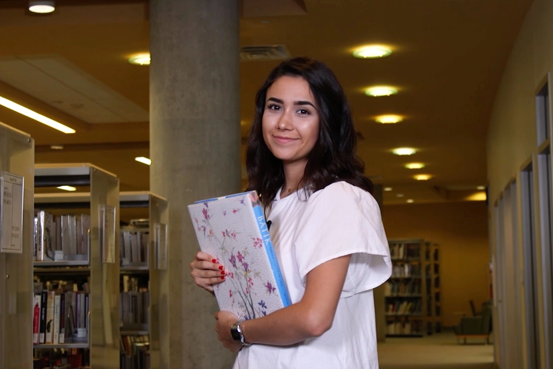 A student holds in a book while in the library at an HCC campus.