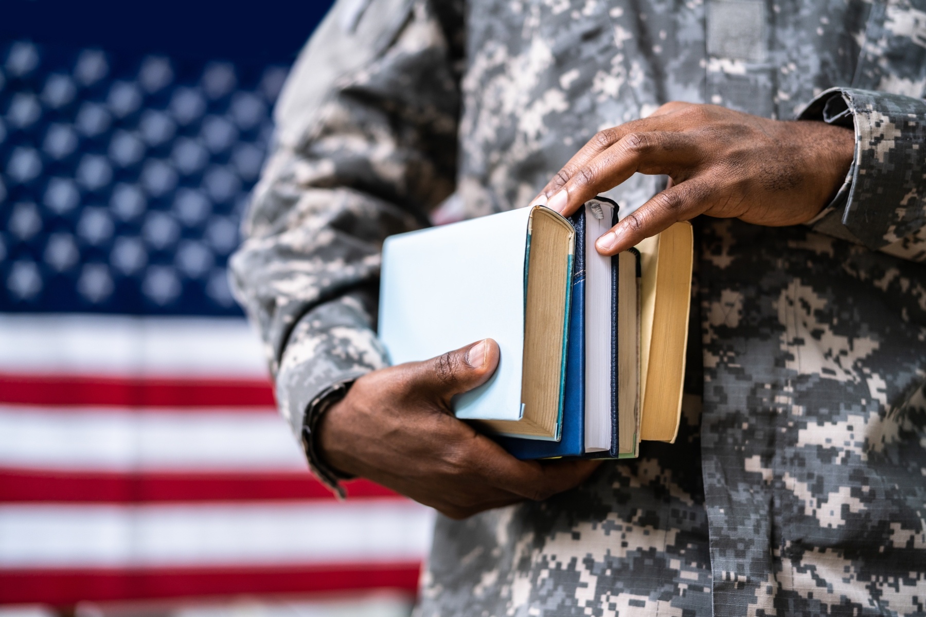 With a United States flag in the background, a member of the military holds some books in his hands.