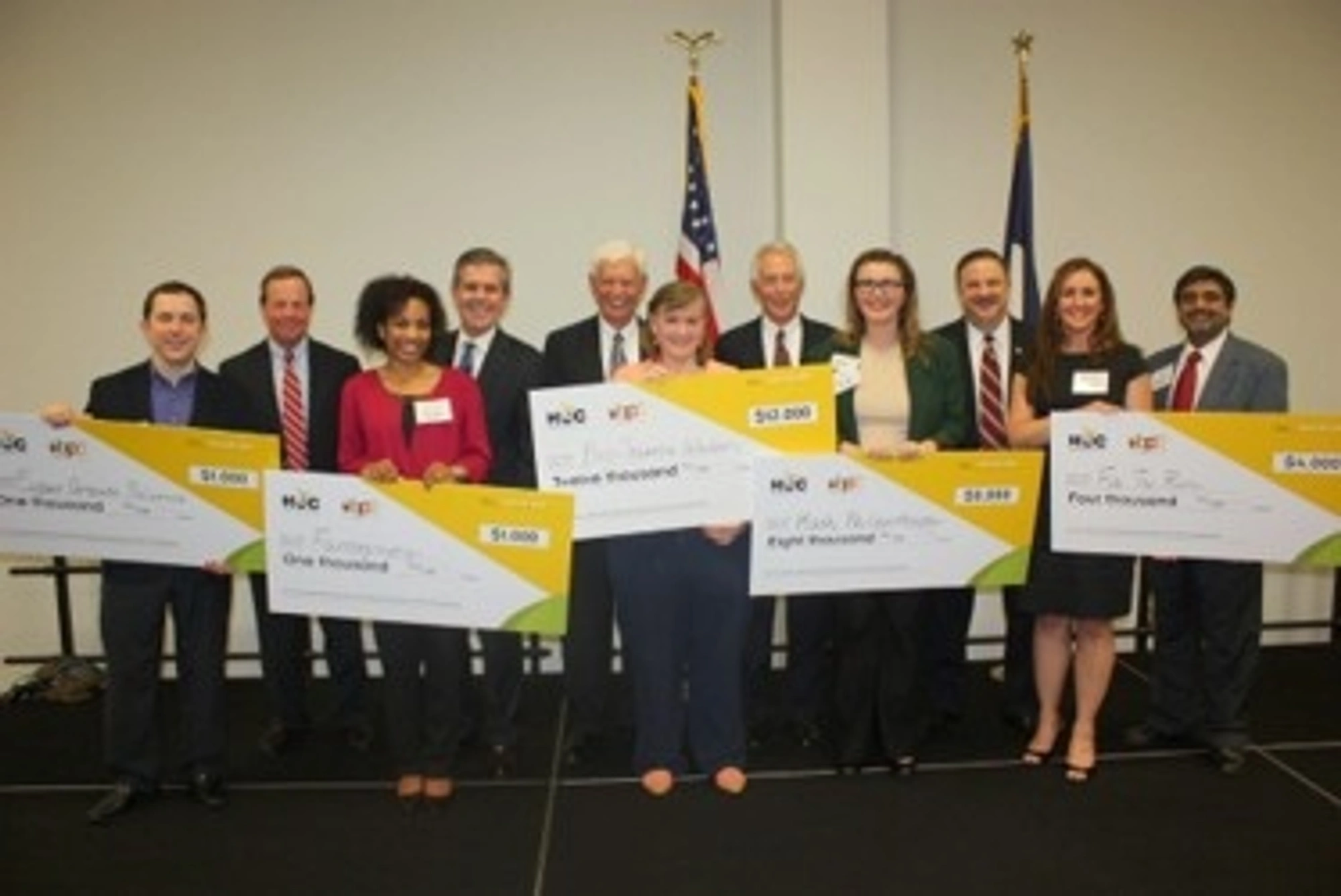 The 2014 Business Plan Competition winners hold large checks as they pose for a group photo during a ceremony.