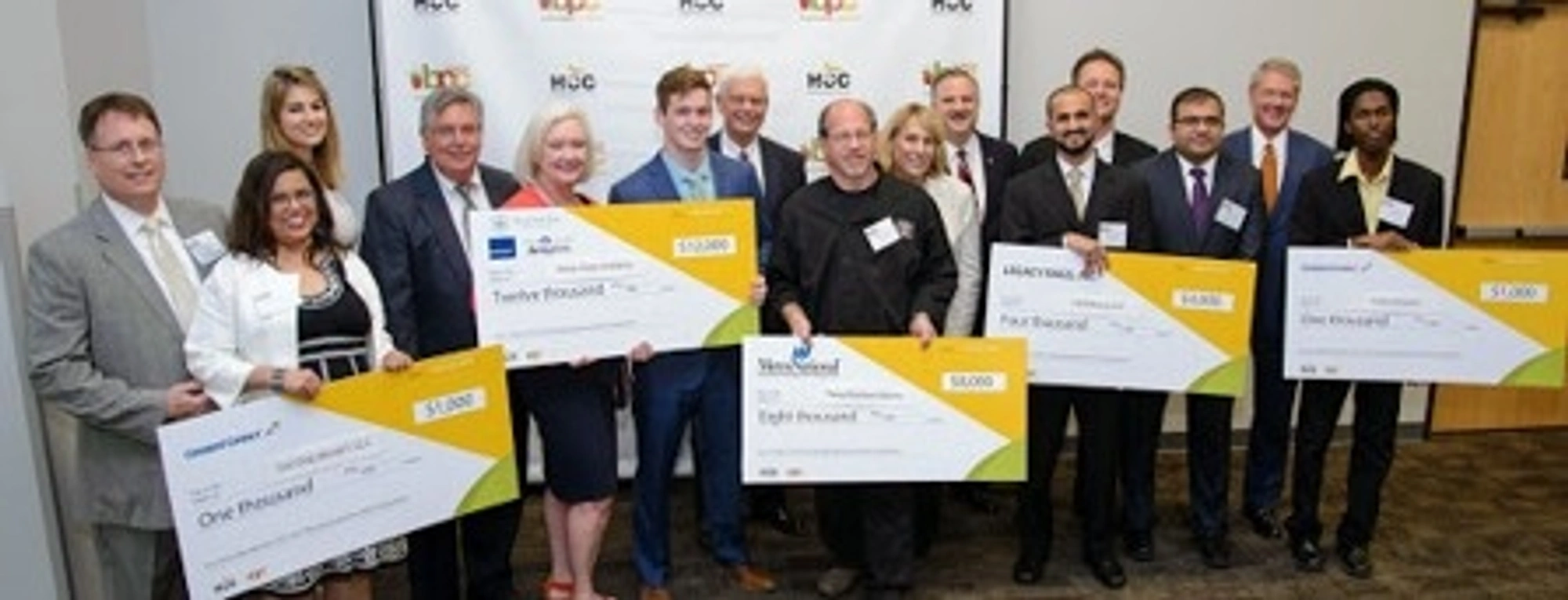 The 2015 Business Plan Competition winners hold large checks as they pose for a group photo during a ceremony.