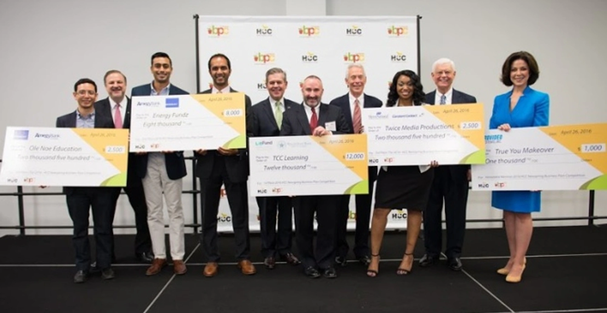 The 2016 Business Plan Competition winners hold large checks as they pose for a group photo during a ceremony.