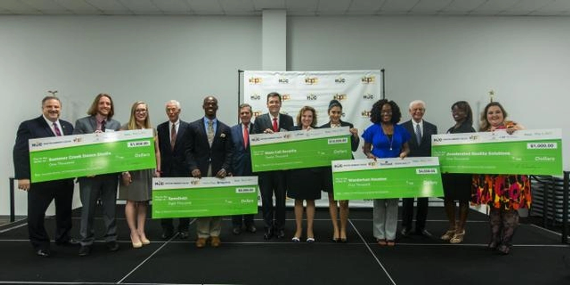 The 2017 Business Plan Competition winners hold large checks as they pose for a group photo during a ceremony.