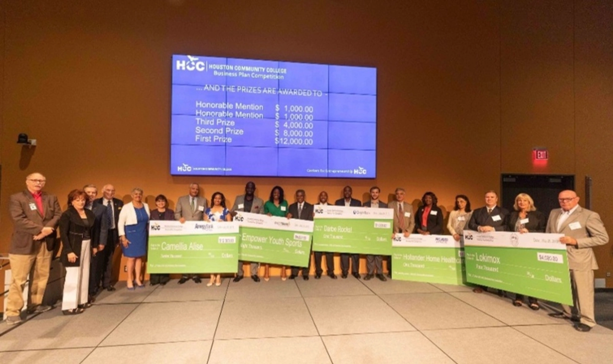 The 2019 Business Plan Competition winners hold large checks as they pose for a group photo during a ceremony.