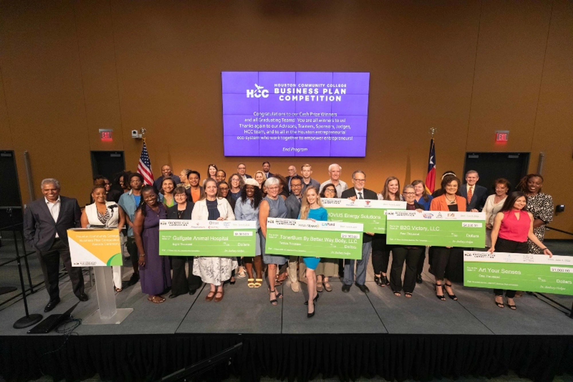 The 2022 Business Plan Competition winners hold large checks as they pose for a group photo during a ceremony.