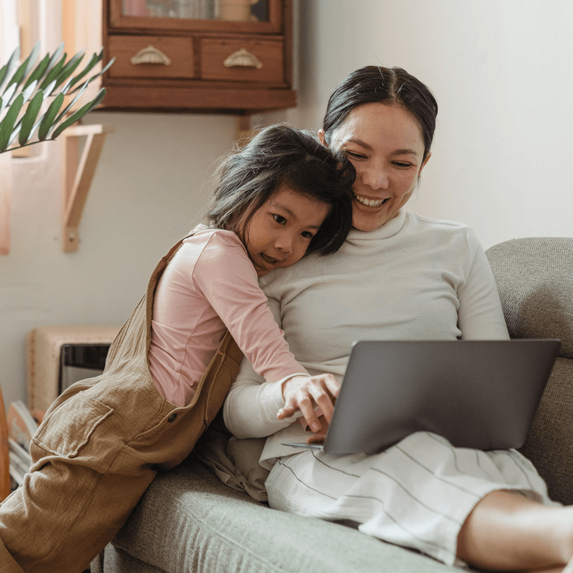 A mother and her young daughter look at a laptop.