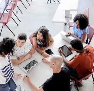Group of students with labtops and tablets sitting at a table on campus