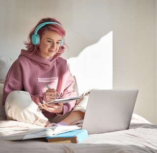 Female student attending an online class from the comfort of her bedroom
