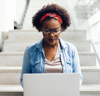 Female student using her laptop on the steps of a campus building.