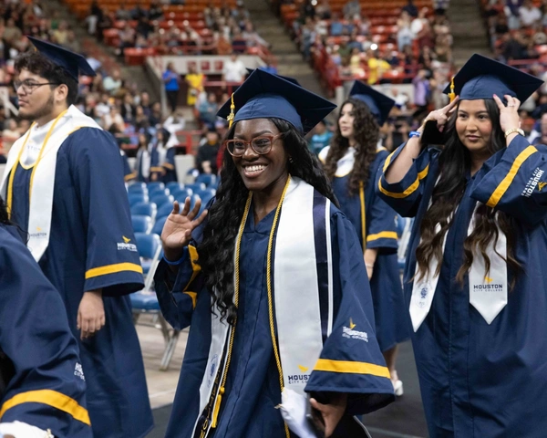 An HCC graduate waves while walking at the Commencement Ceremony.