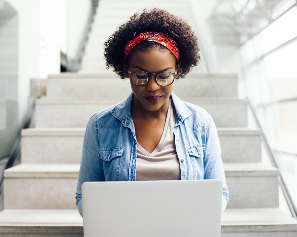 Female student using her laptop on the steps of a campus building.