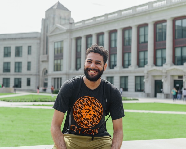 Male student sitting in front of a college building