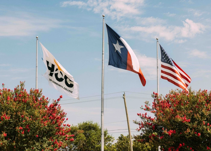 The United States of America, Texas, and HCC flags waving on a flag post on campus