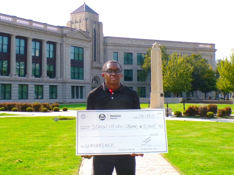 Simon Obame stands in front of the HCC Central Campus holding a scholarship check from the International Society of Automation, Houston Section.